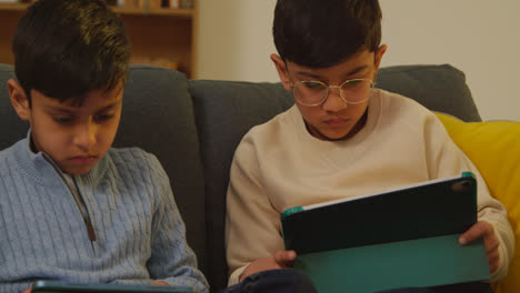 Zwei-Junge-Jungen-Sitzen-Zu-Hause-Auf-Dem-Sofa-Und-Spielen-Spiele-Oder-Streamen-Auf-Digitale-Tablets-4